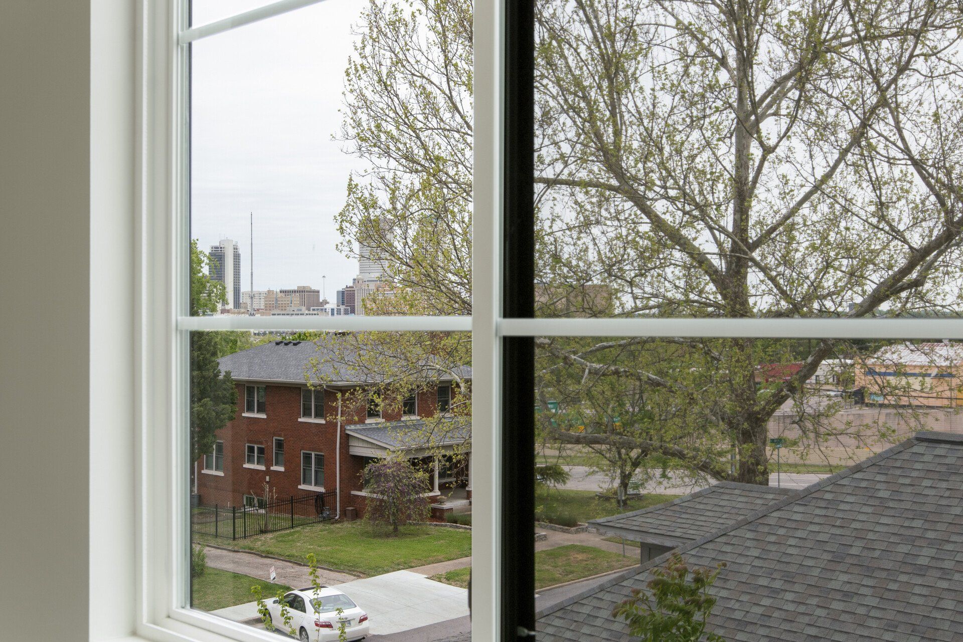 A window with a view of a brick house and a tree.