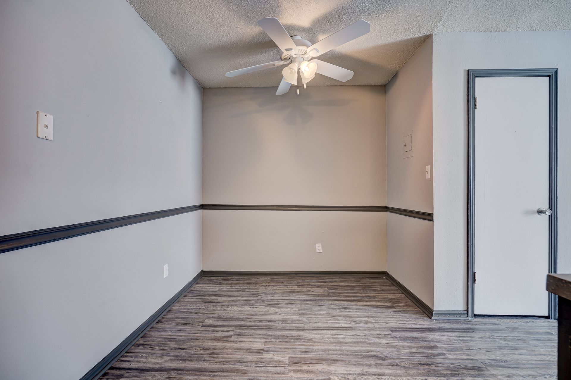An empty room with a ceiling fan and a door.