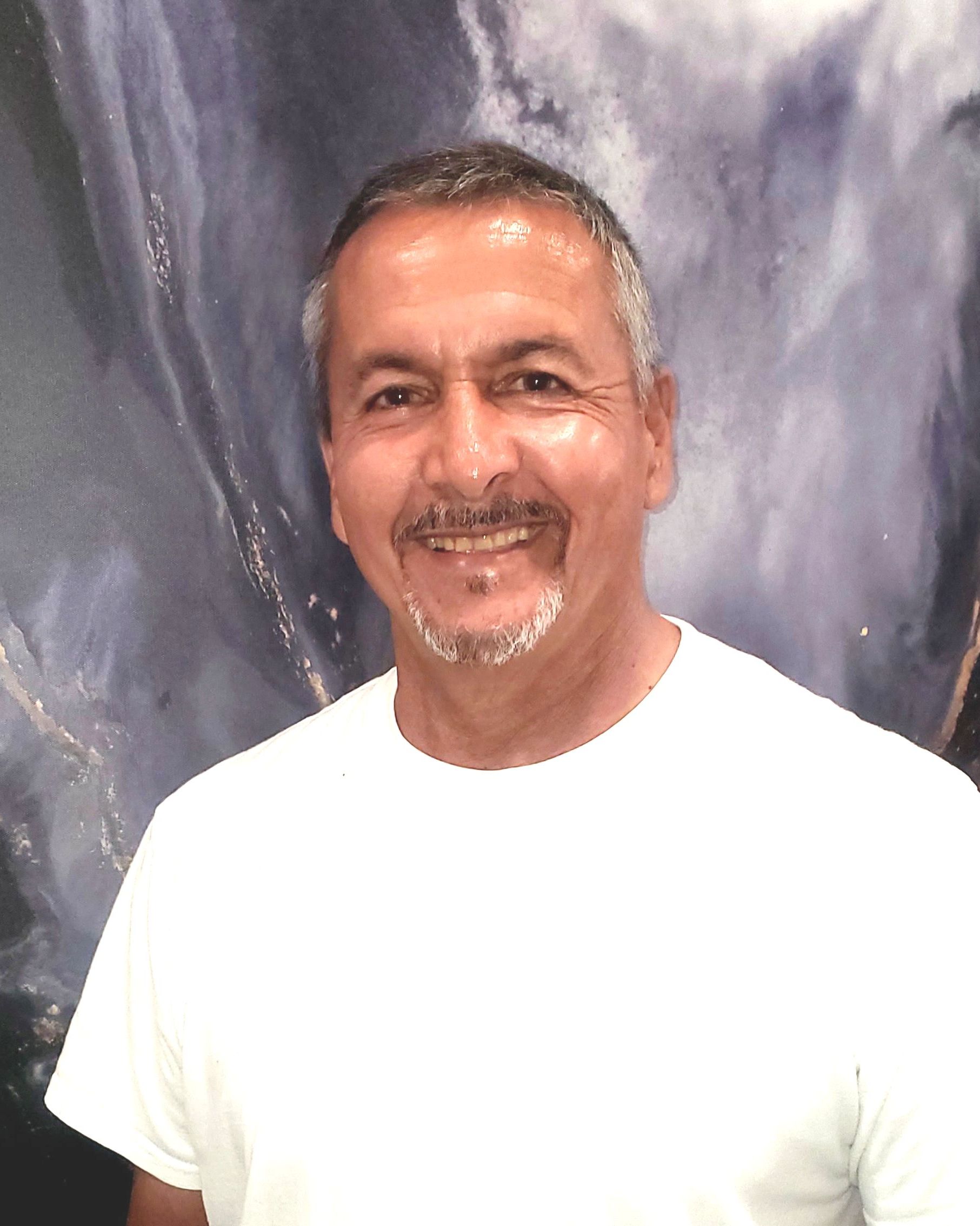 A man in a white shirt is smiling in front of a painting