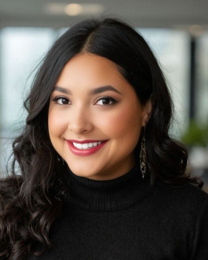 A woman wearing a black turtleneck and earrings is smiling for the camera.