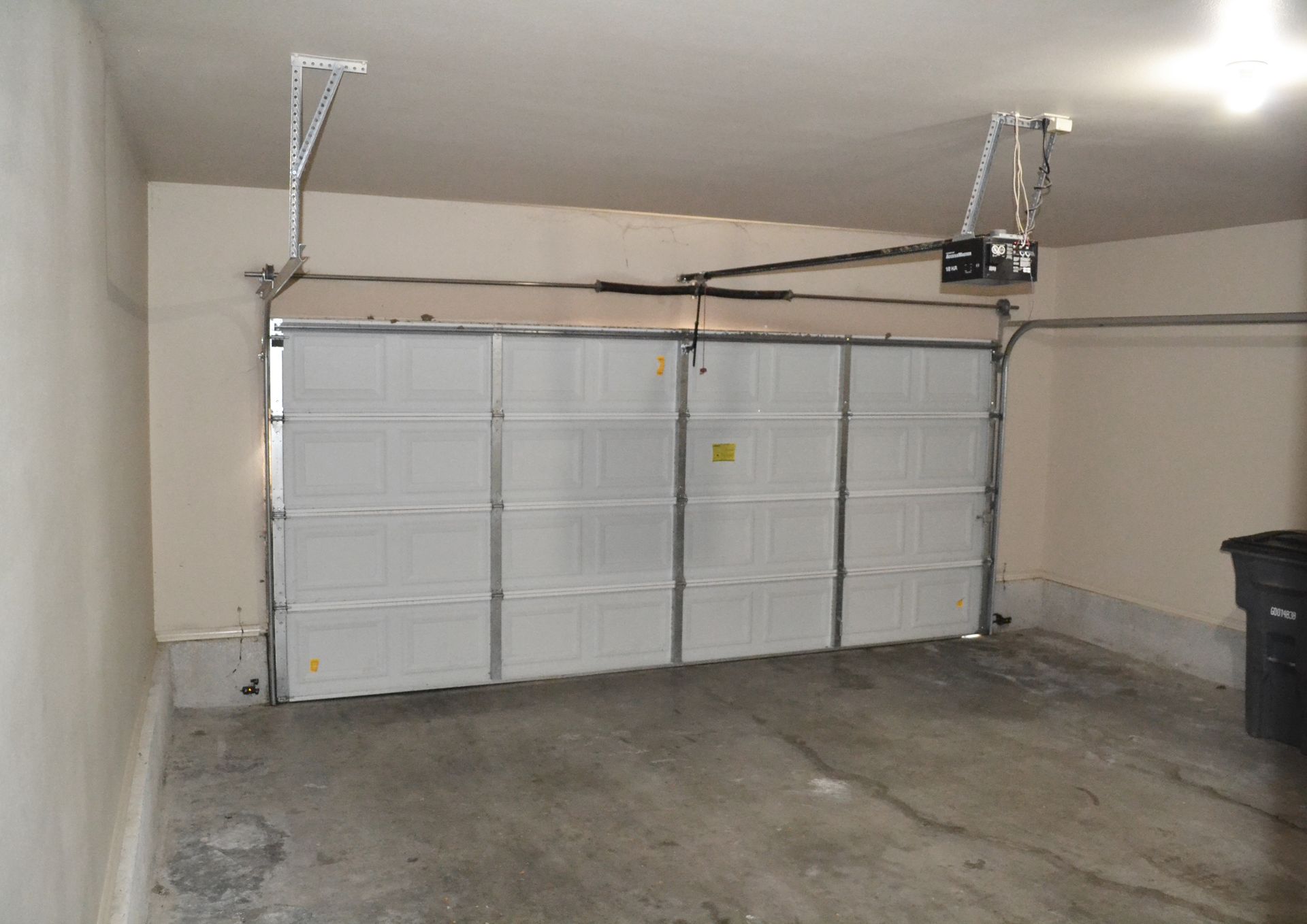 A garage with a white garage door and a black trash can