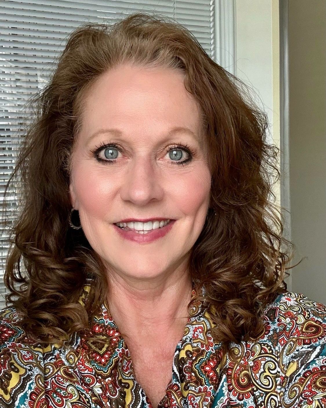 A woman with long brown hair and blue eyes is smiling for the camera.