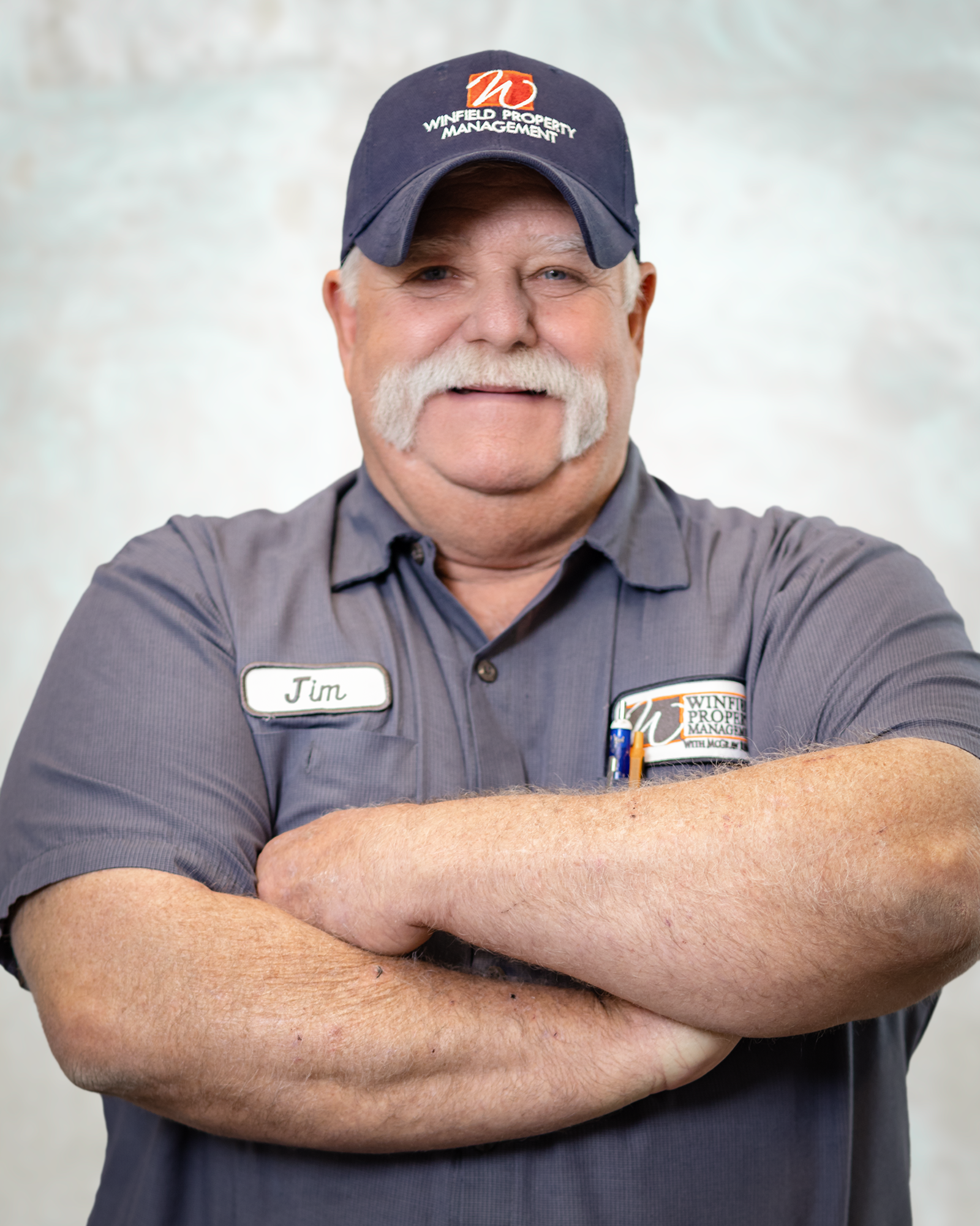 A man with a mustache and a hat is standing with his arms crossed.