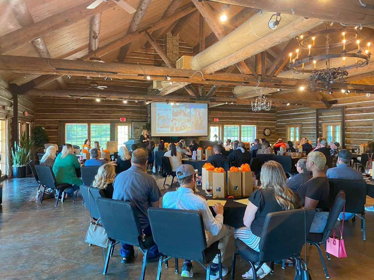 A group of people are sitting at tables in a room with a projector screen.