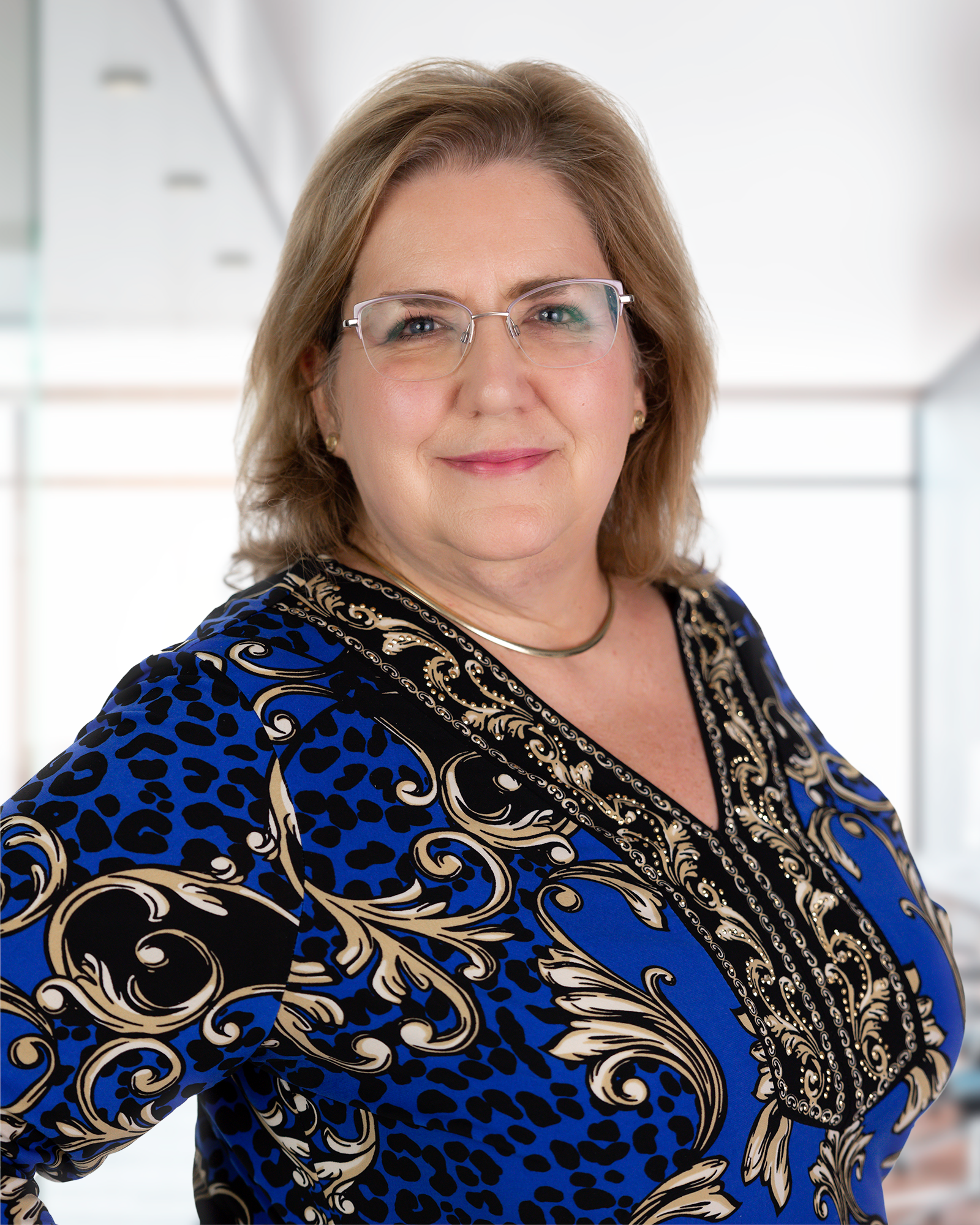 A woman wearing glasses and a blue and black shirt is standing in front of a window.