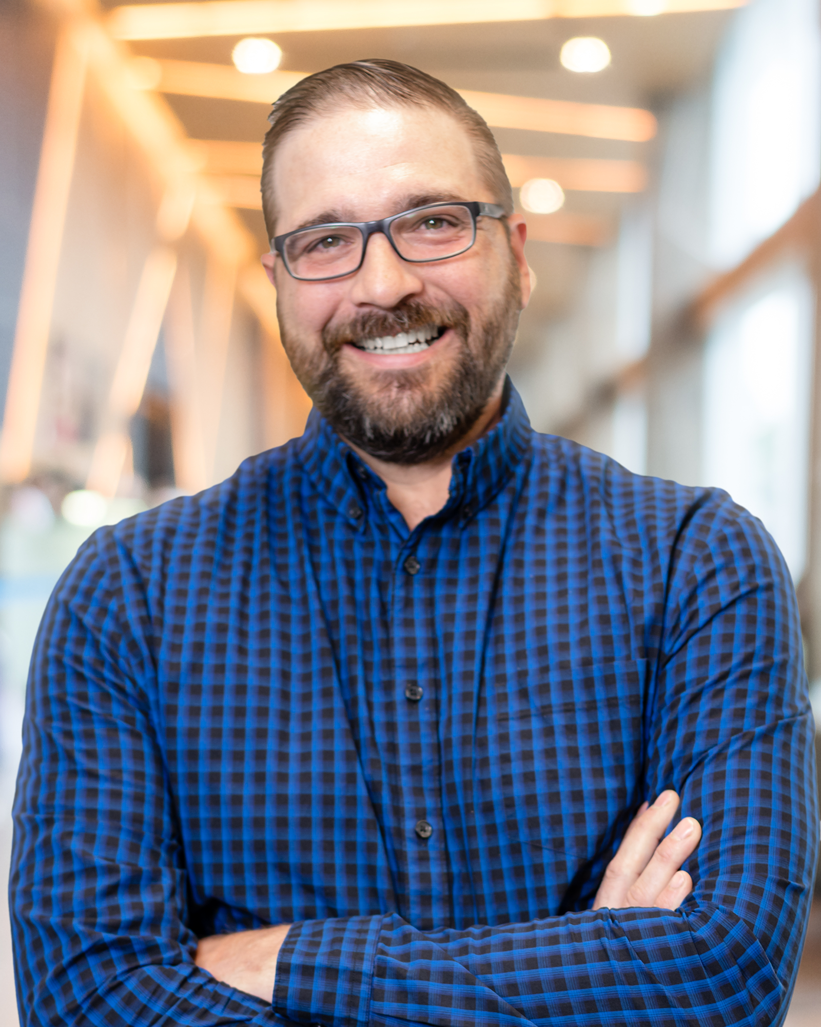 A man with a beard and glasses is smiling with his arms crossed.
