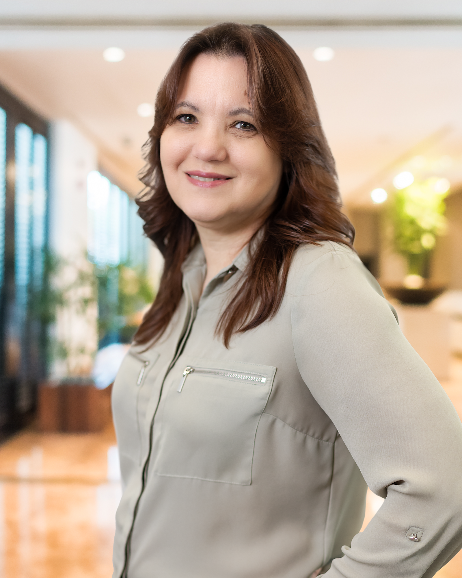 A woman is standing in a room with her hands in her pockets and smiling.