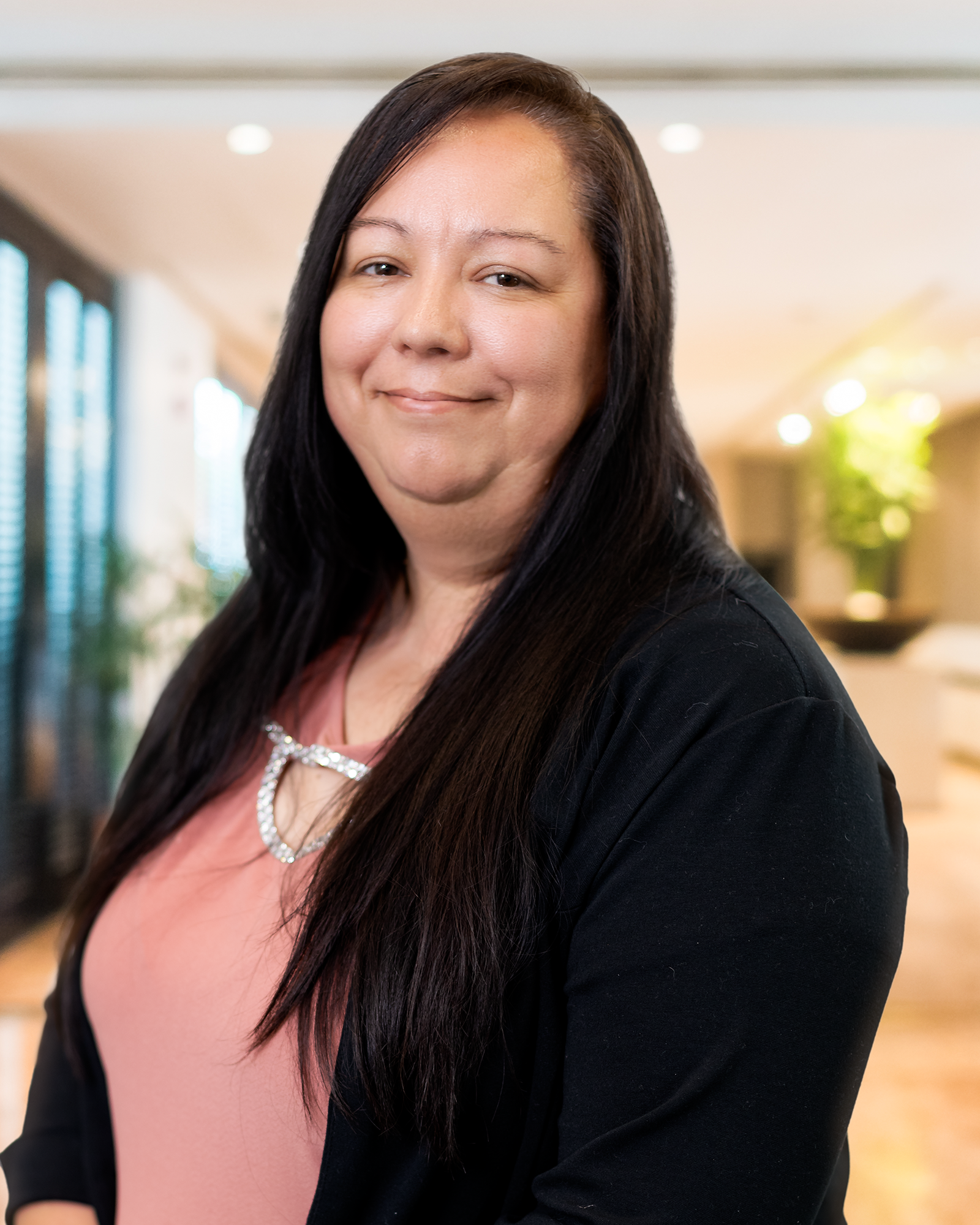 A woman in a pink shirt and black sweater is smiling for the camera.