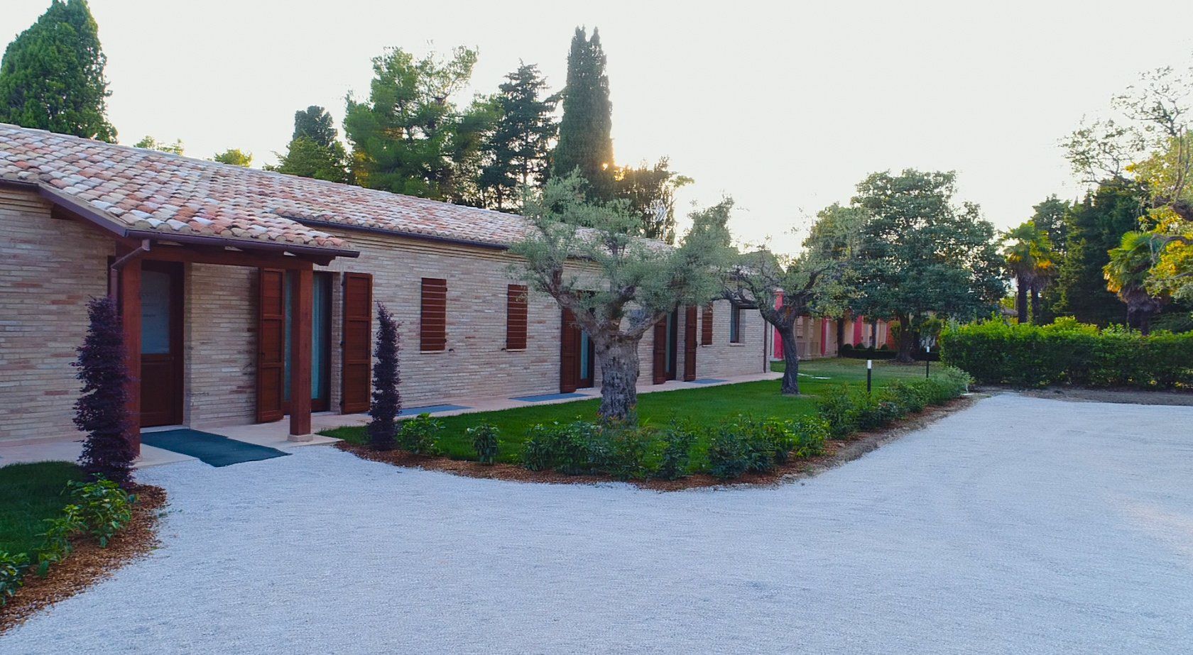 una casa di mattoni con un tetto di tegole è circondata da alberi e arbusti