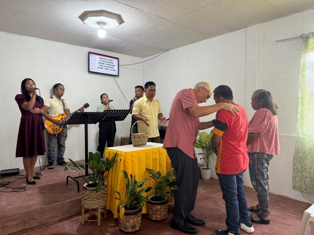 People in a church service with a man being blessed. A band plays in the background.