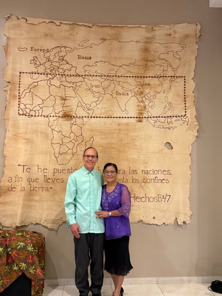 A couple posing in front of a world map on a wall. The map is drawn on parchment.