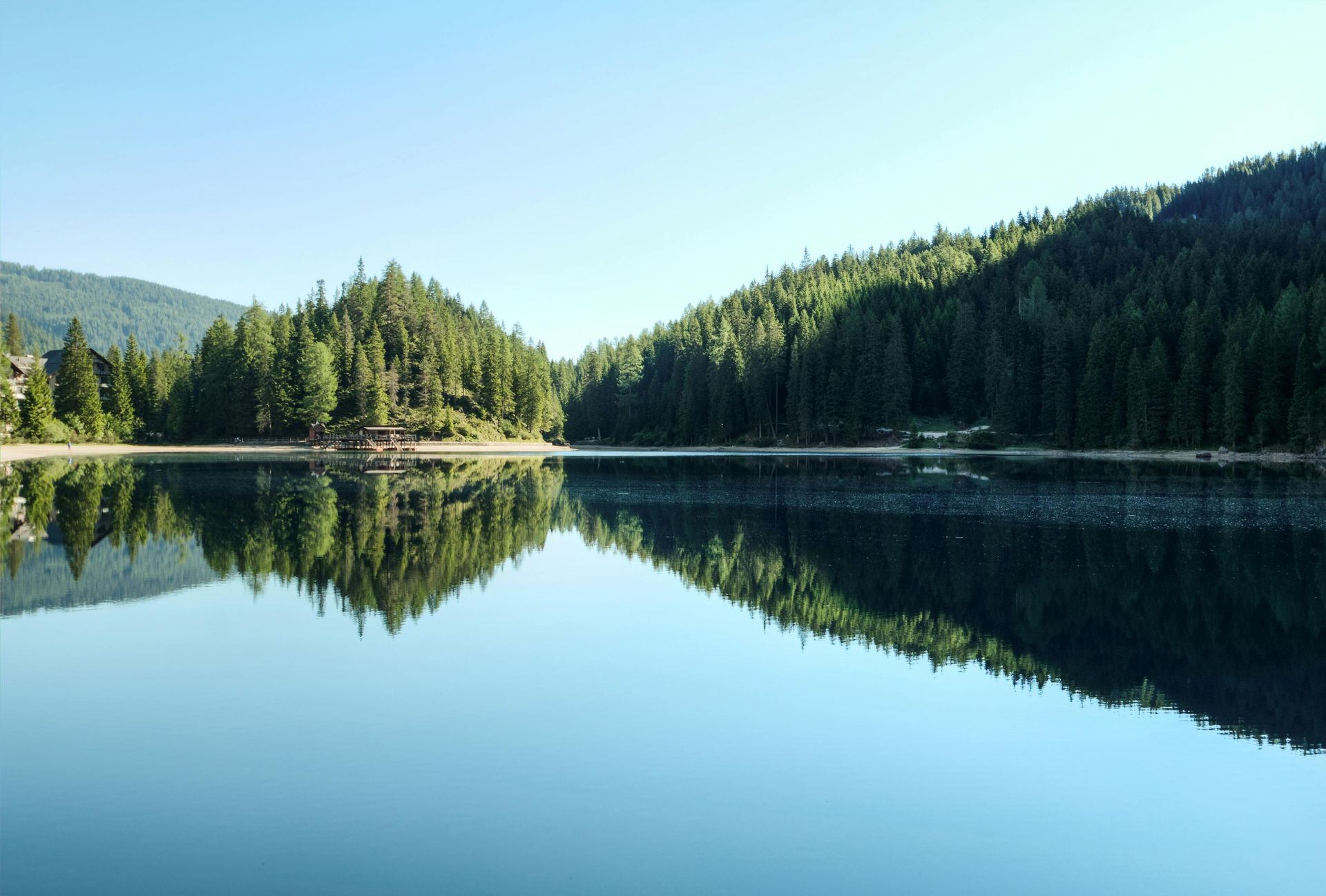 Still lake reflects evergreen trees and blue sky.