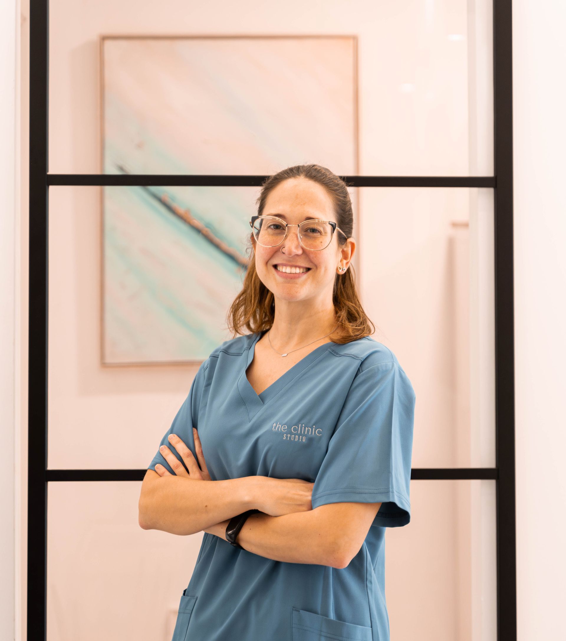 Una mujer con un uniforme azul está parada frente a una ventana con los brazos cruzados.