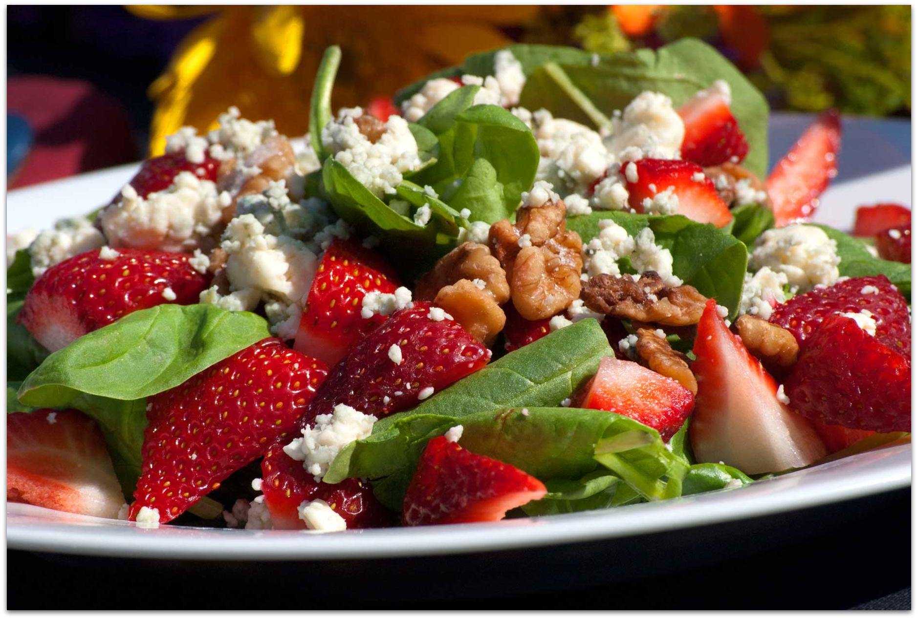 A salad with strawberries spinach cheese and walnuts on a white plate