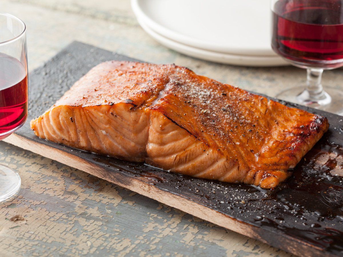 A piece of salmon is sitting on a wooden cutting board next to a glass of wine.