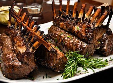 A white plate topped with lamb chops and rosemary on a table.