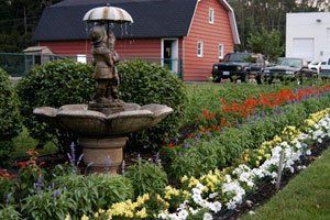 A fountain in a garden with a red barn in the background.