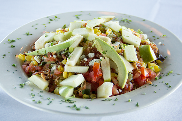 A white plate topped with a salad of vegetables and avocado slices.