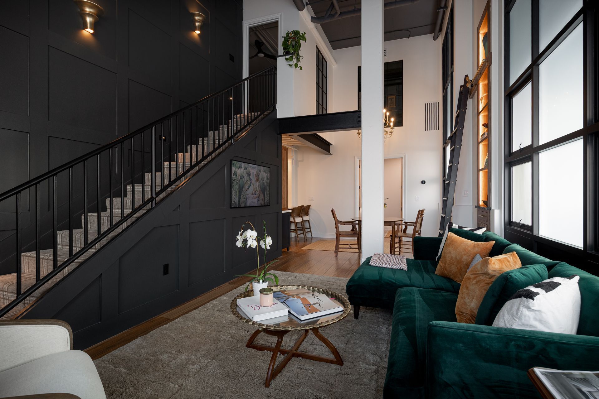 Living room with dark gray walls, staircase, emerald sofa, and large windows.