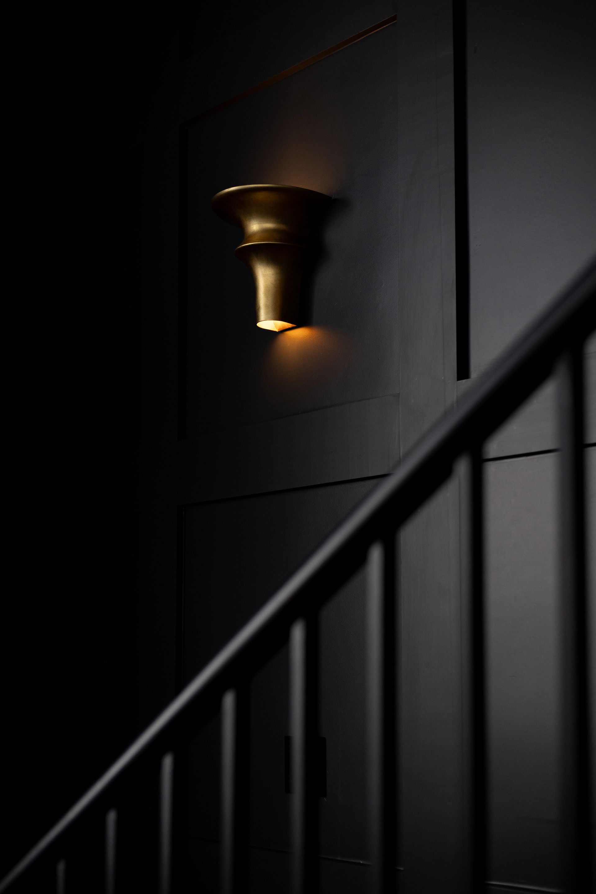 Gold sconce on a dark wall next to a staircase.