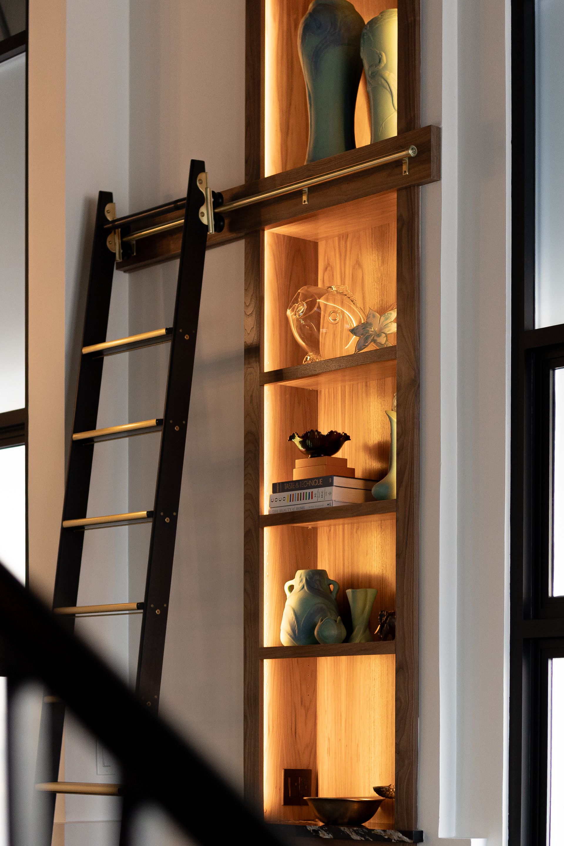 Wooden bookshelf with built-in lighting, ladder. Displaying vases and decorative objects.