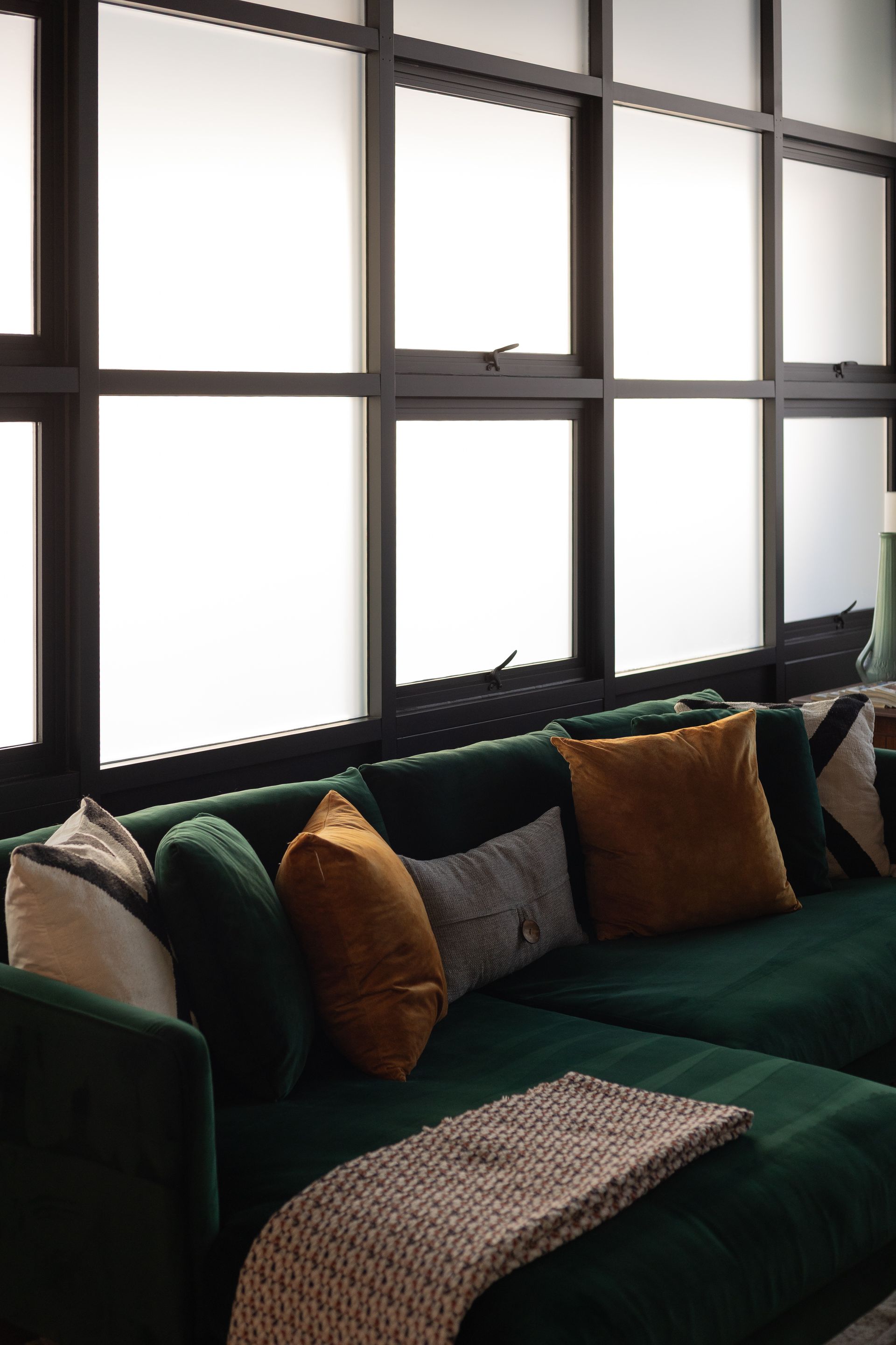 Green sectional sofa with several pillows in front of large frosted windows.