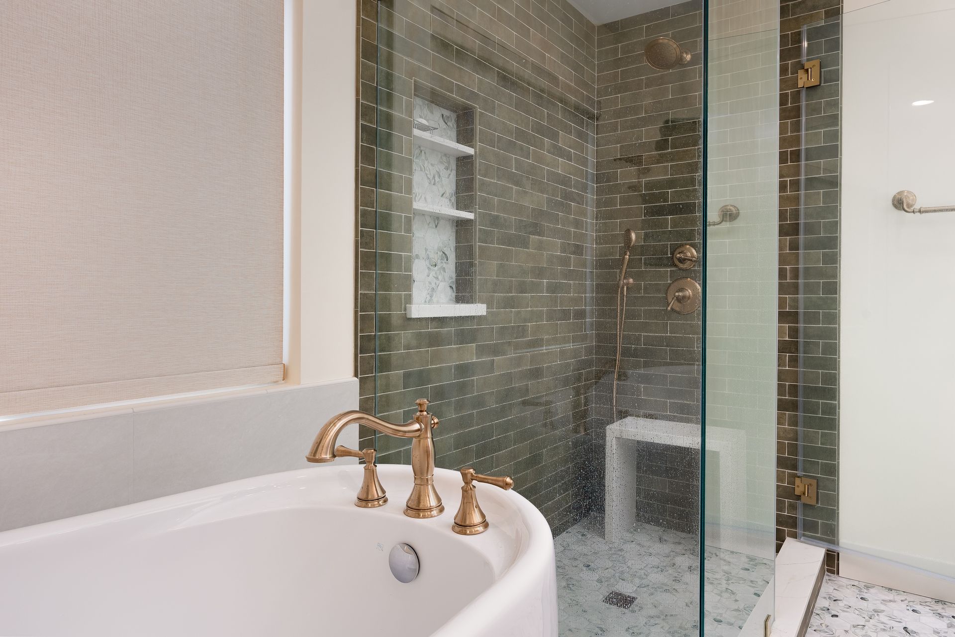 Bathroom with a white bathtub, gold faucet, and a glass shower with dark green tile.