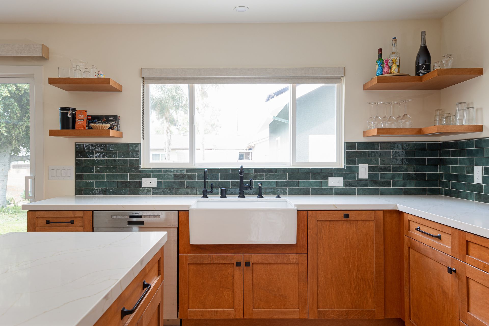 Kitchen with wooden cabinets, white sink, green tile backsplash, and floating shelves.