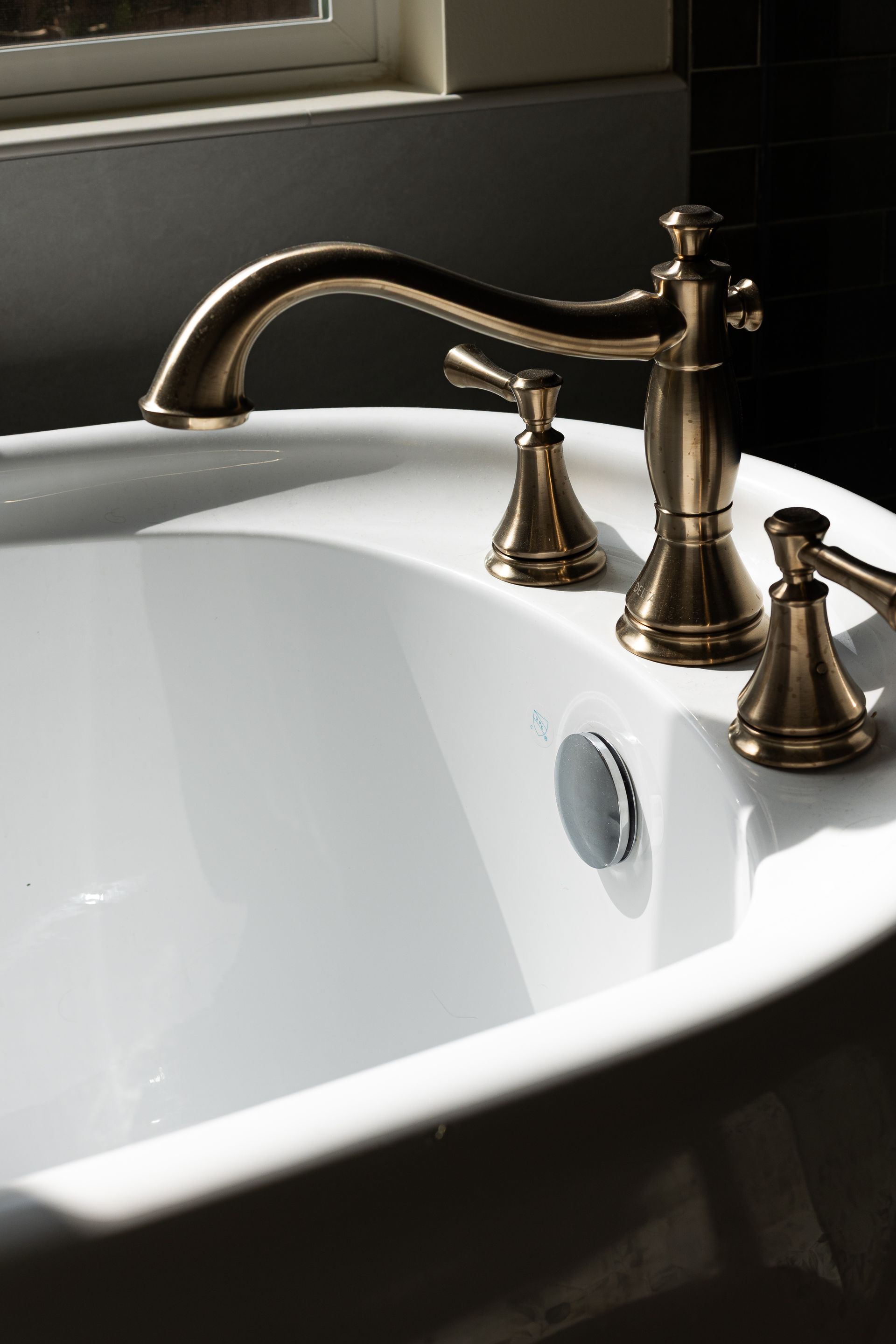Antique brass faucet on a white bathtub, sunlight highlights the fixtures.