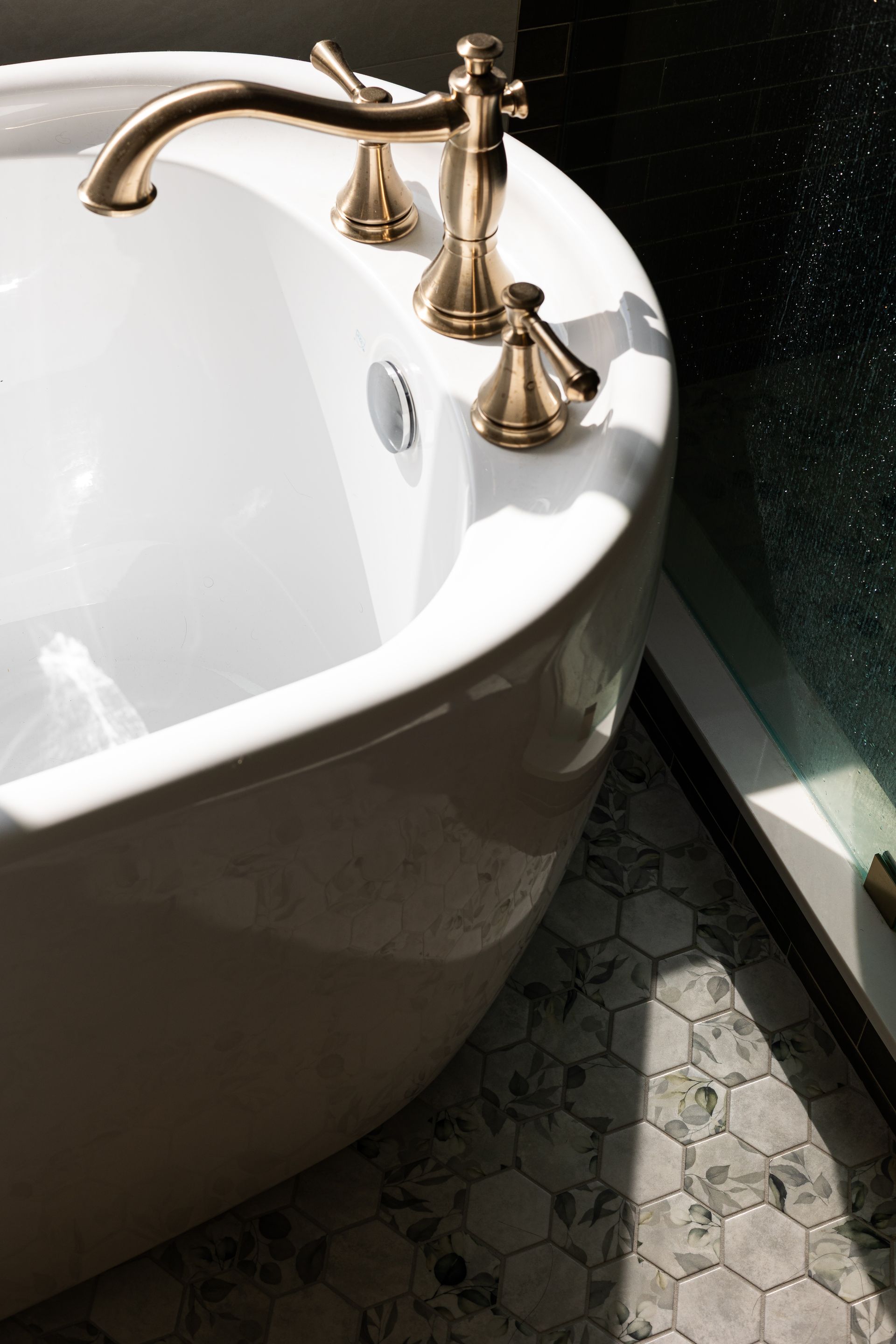 White bathtub with gold fixtures, on patterned tile floor, near window.