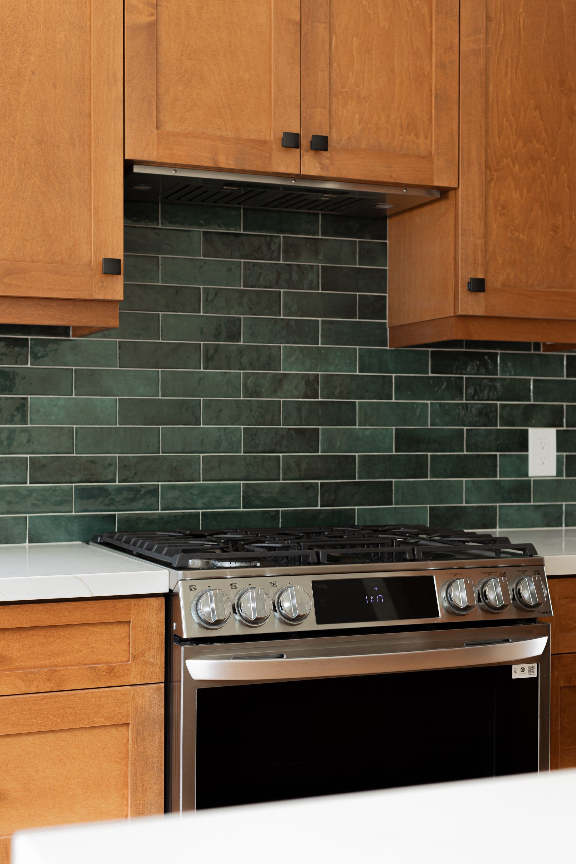 Stainless steel oven and stove against green subway tile backsplash and wood cabinets.