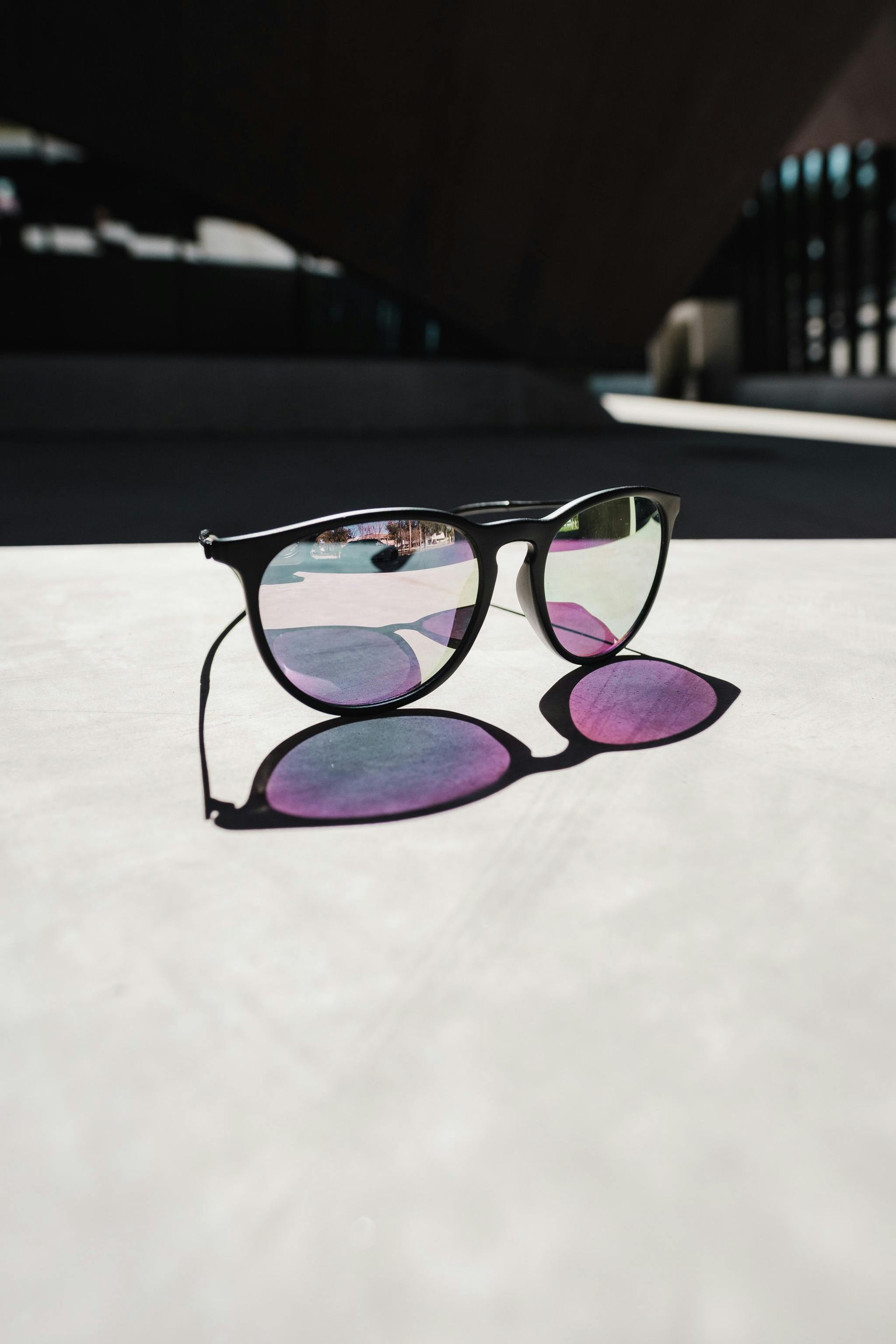 Black sunglasses with purple-tinted lenses cast a shadow on a bright white surface.