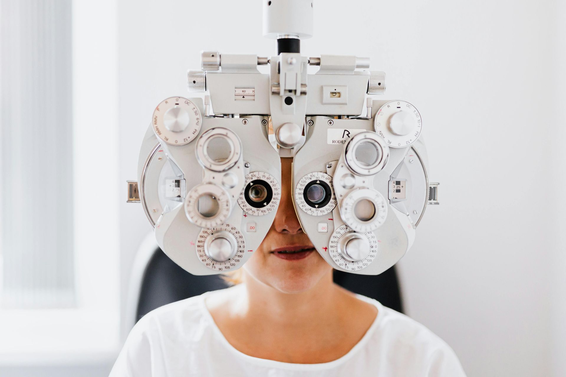 Woman with head in an eye exam machine, looking forward in a white room.