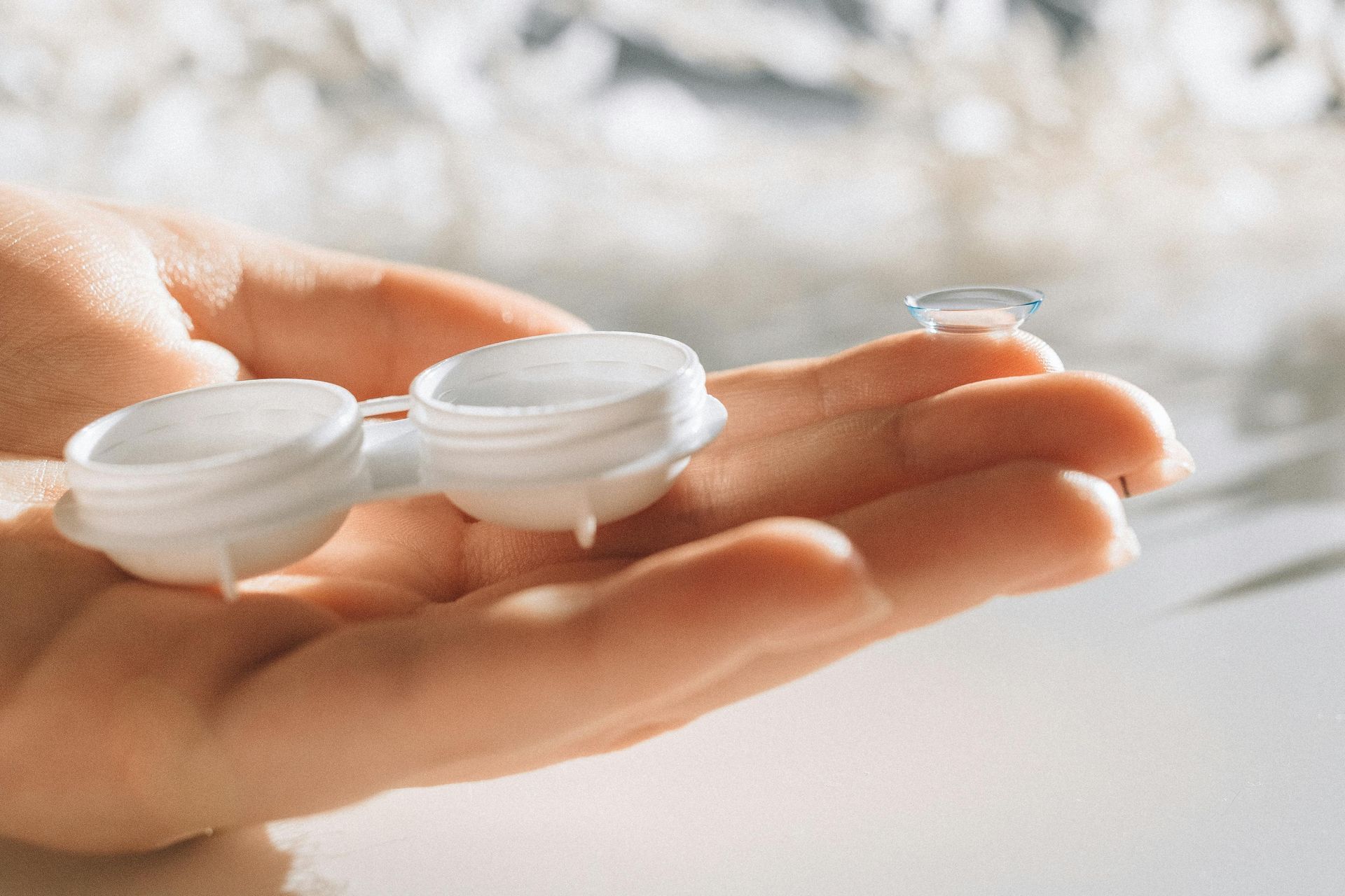 Hand holding a white contact lens case and a single contact lens.