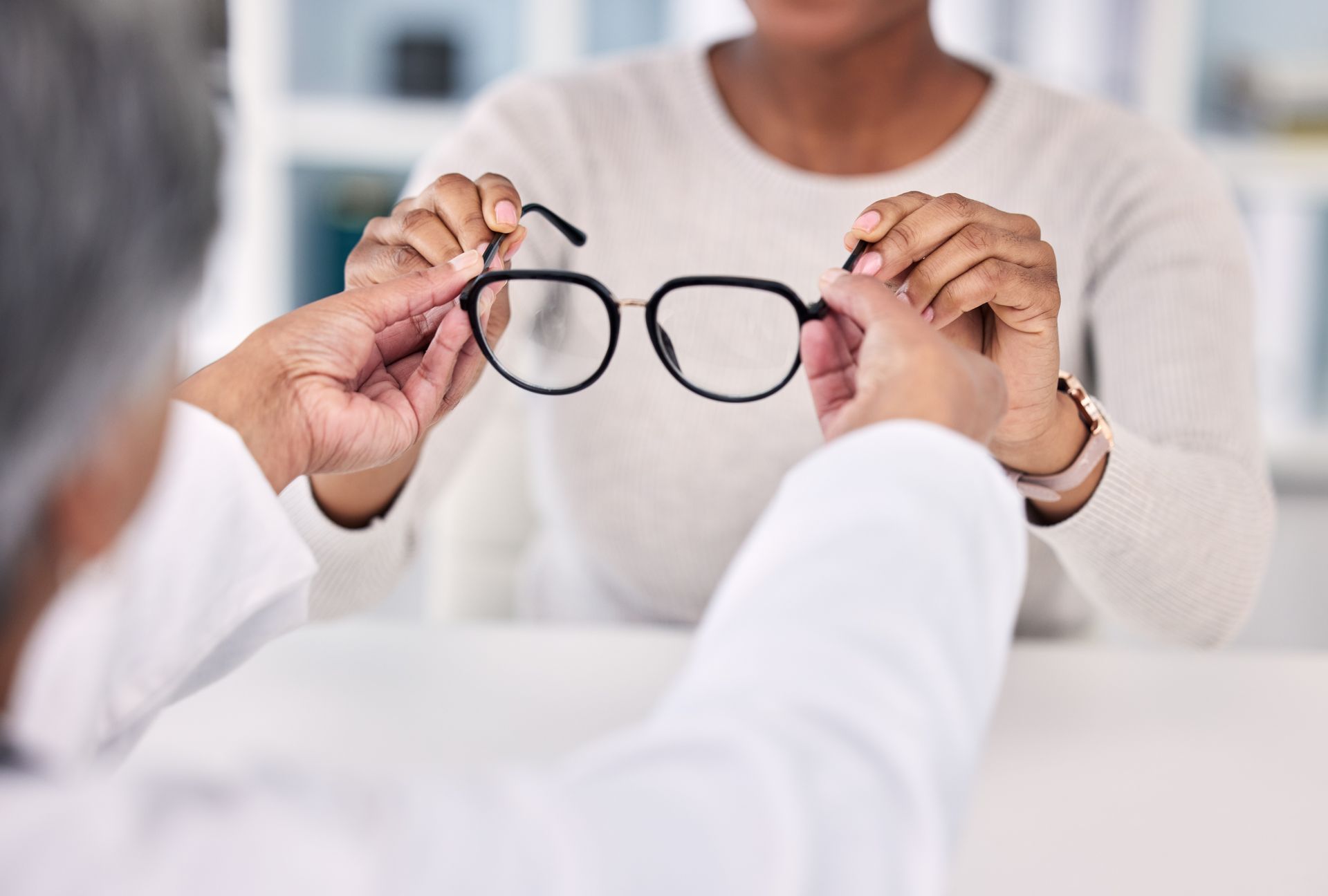 Optometrist hands eyeglasses to a patient, indoors.