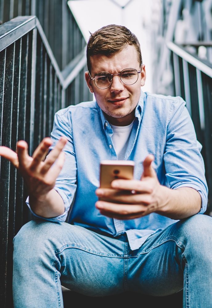 Een man zit op een trap en kijkt op zijn mobiele telefoon.