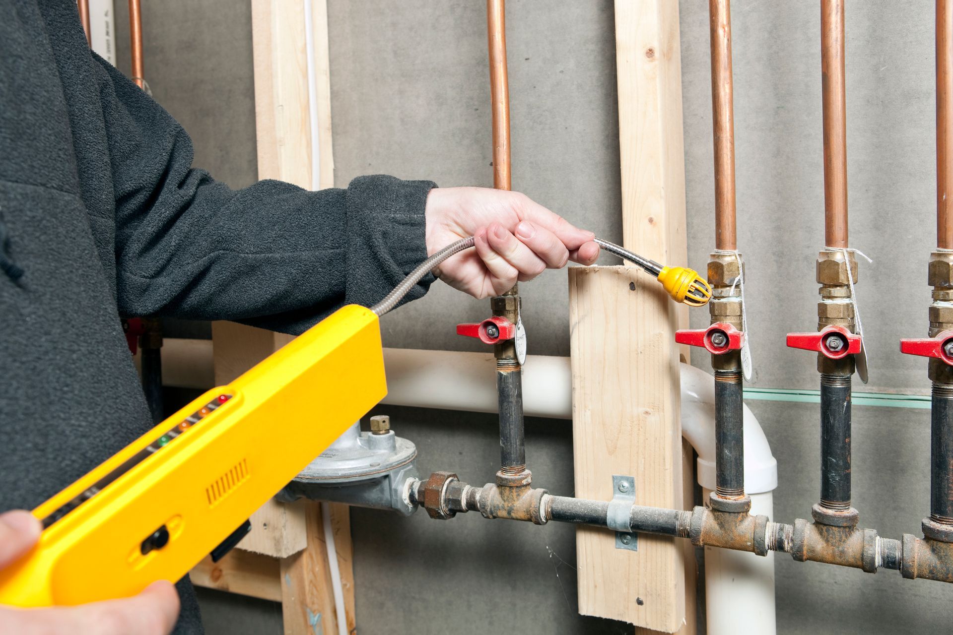 Worker uses a gas detector machine close to copper gas pipes in a home, searching for gas leaks.