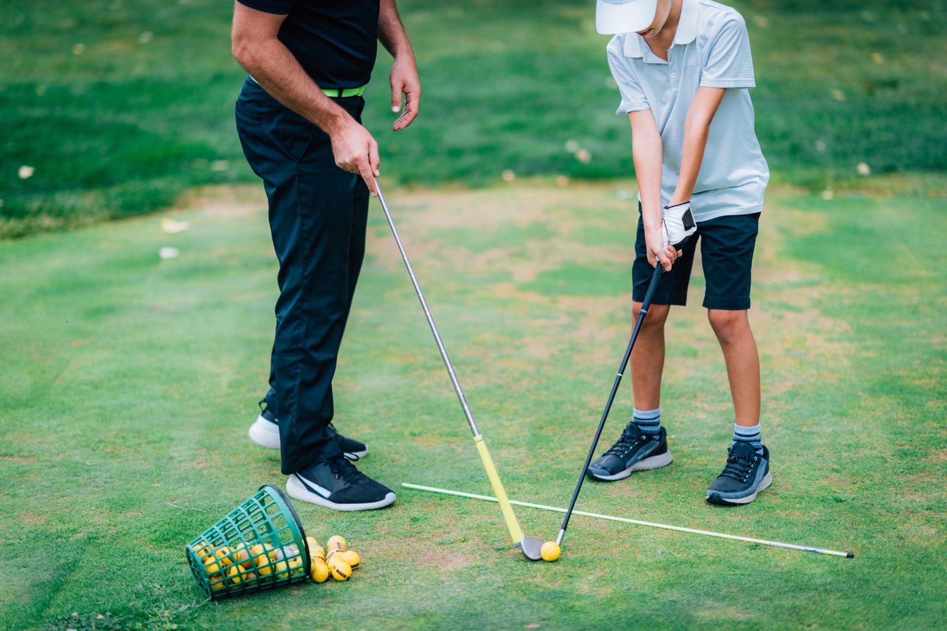 Golf instructor coaching a child on a green, using golf clubs and training aids.