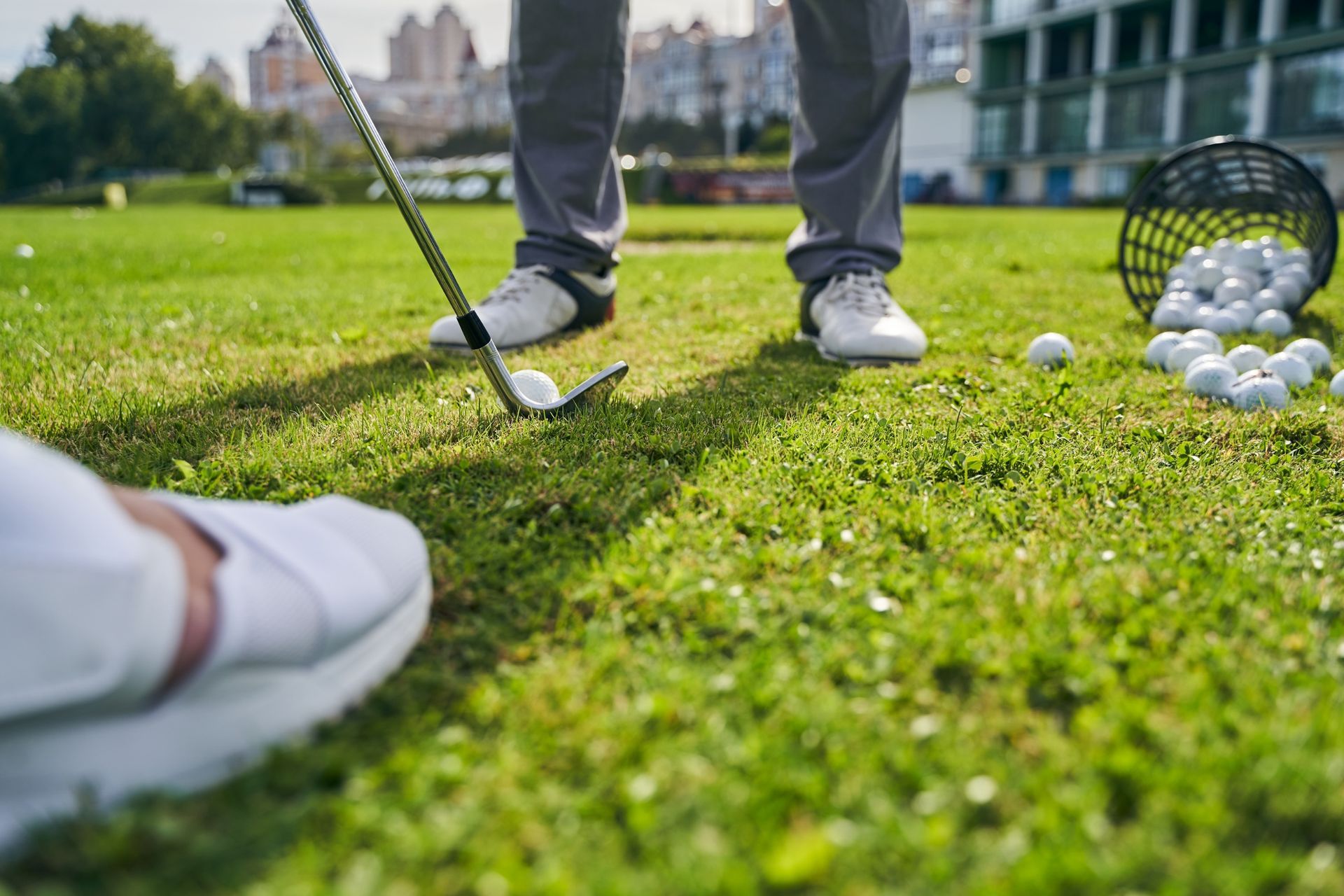 Person golfing on a green with a golf club and ball. Golf balls and a basket are nearby.