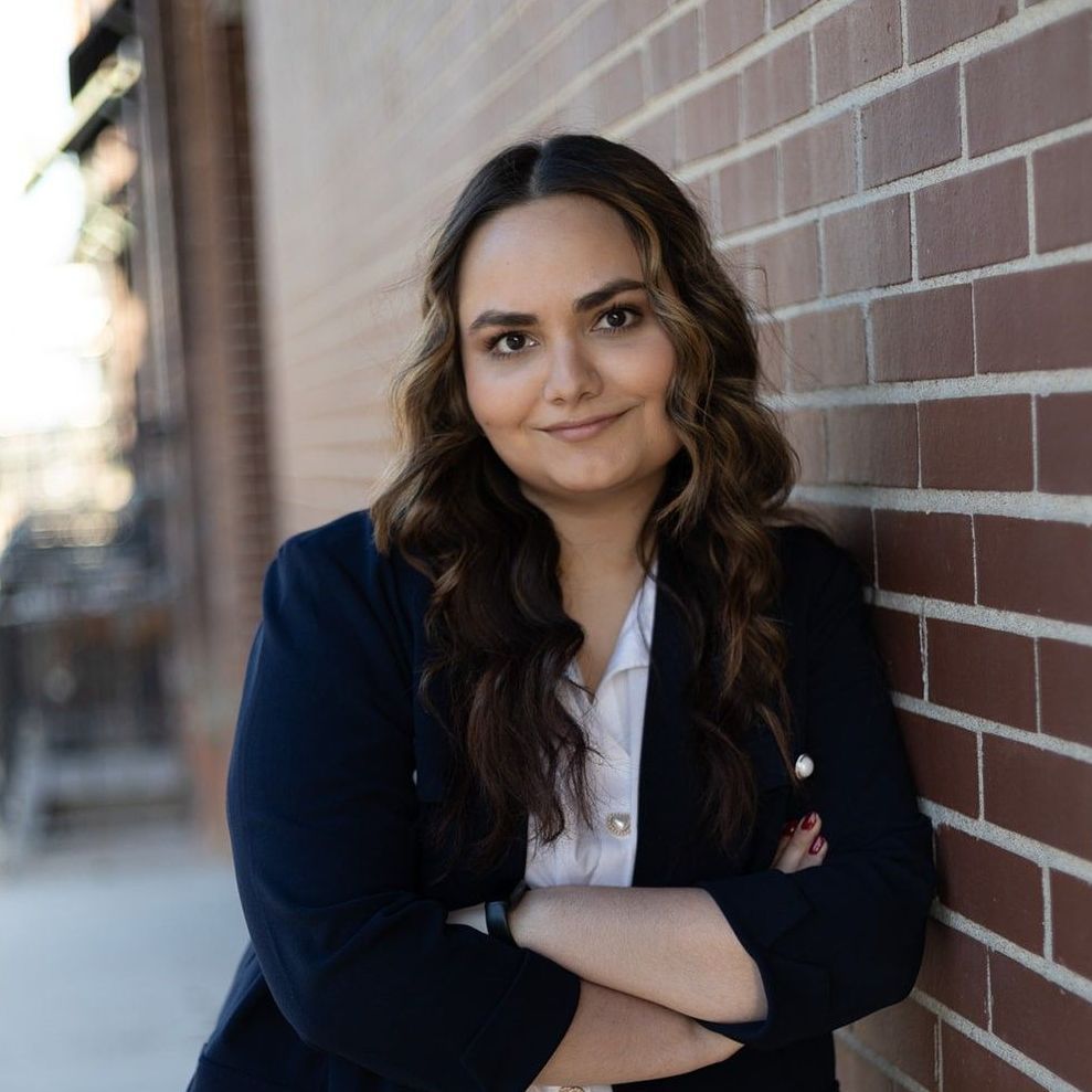A woman is leaning against a wall and smiling for the camera.