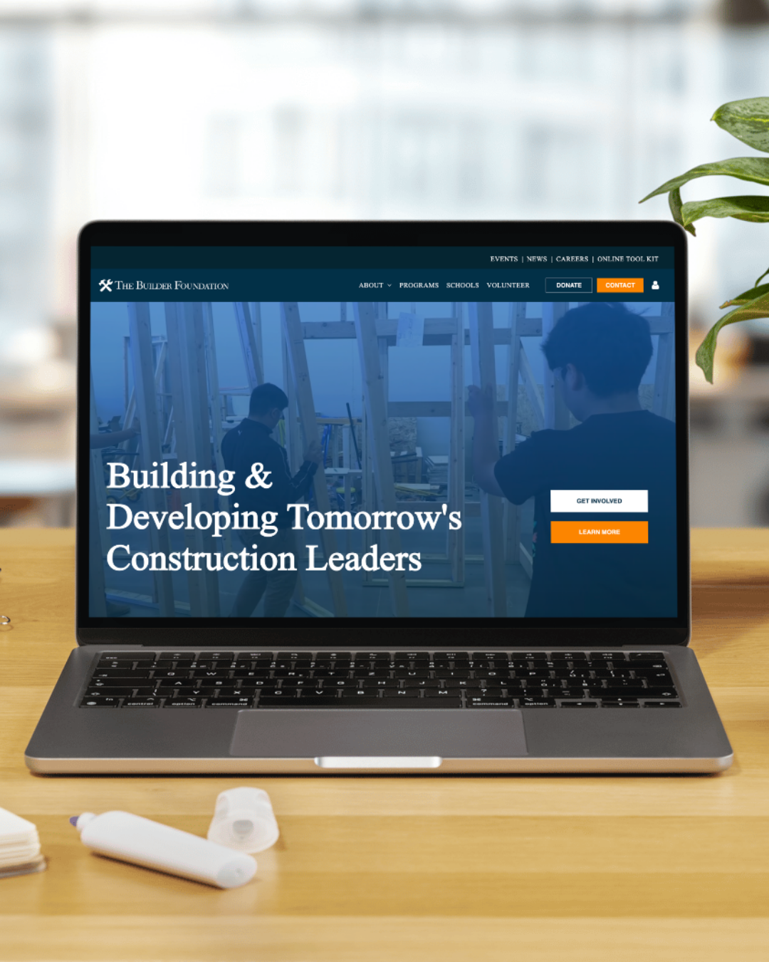 A laptop on a pedestal displays the Adp home page featuring two people in red aprons, set against a dark gray background.