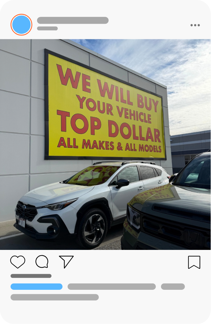 Car dealership lot with a yellow sign reading “We will buy your vehicle top dollar” above parked cars.
