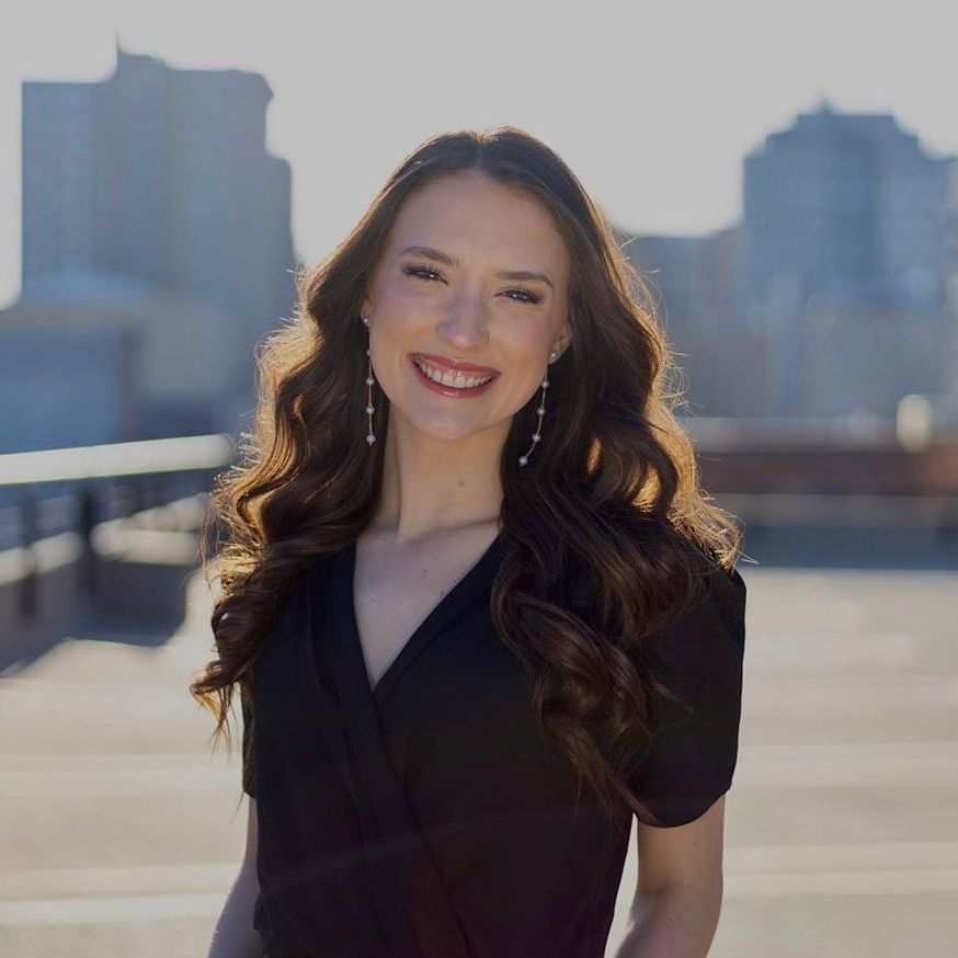 A woman in a grey sweater is smiling for the camera.