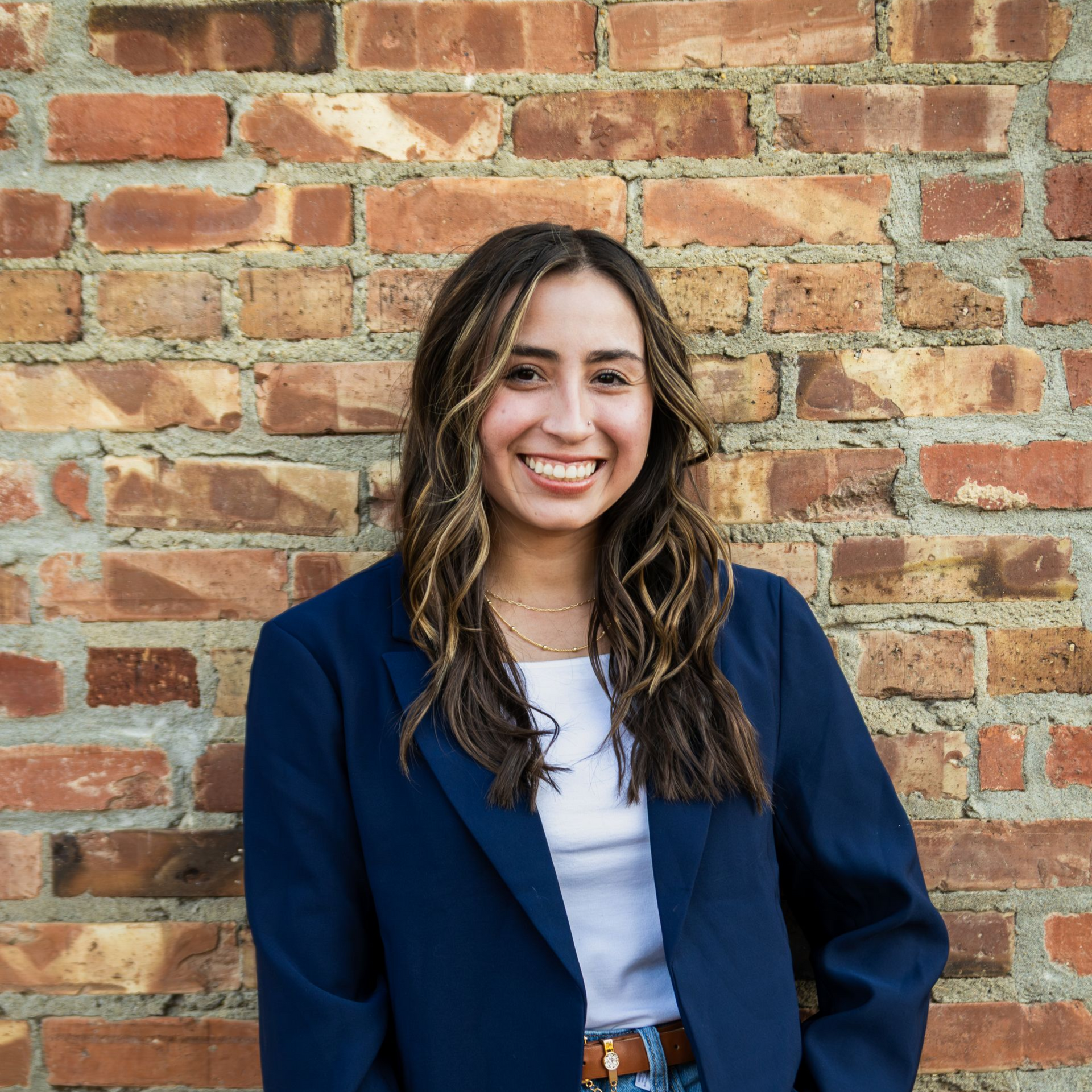 A woman in a floral dress is smiling in front of trees