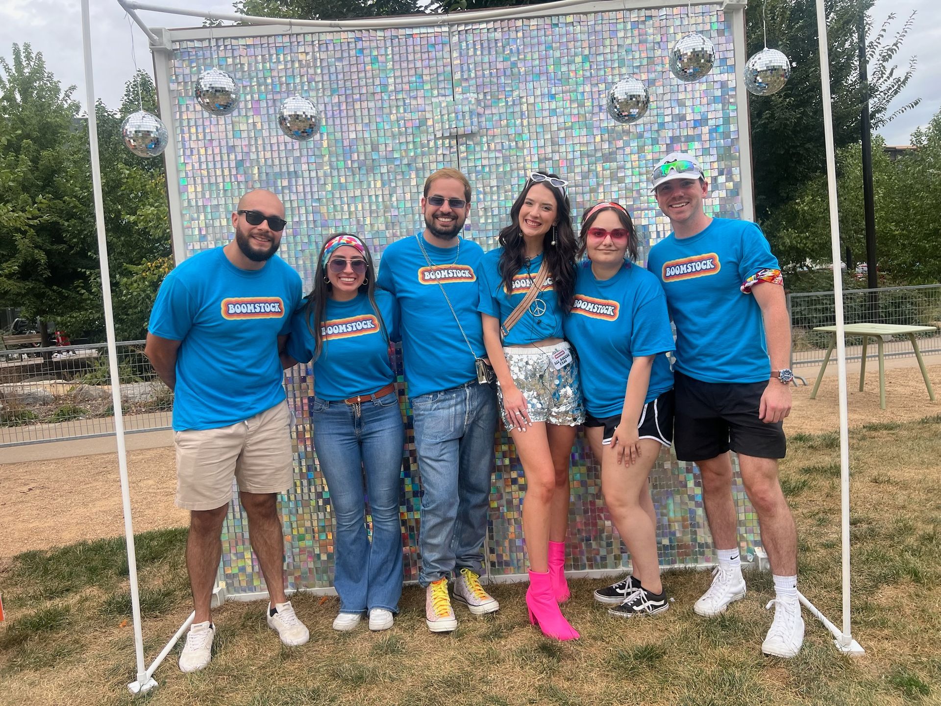 A group of people are posing for a picture in front of a disco ball wall.