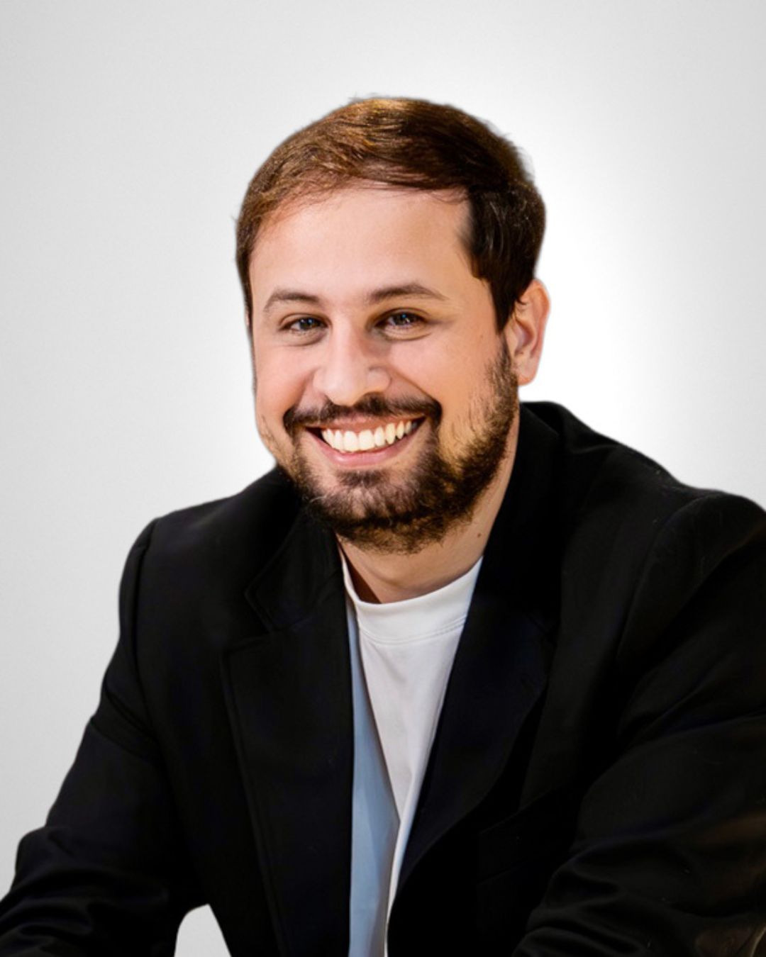 A man with a beard is wearing a black jacket and smiling for the camera.