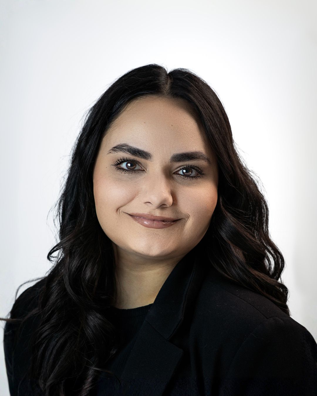 A woman is leaning against a wall and smiling for the camera.