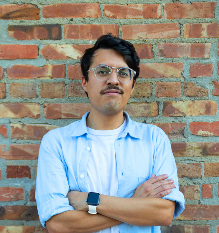 A man wearing glasses and a hat is smiling in a black and white photo.