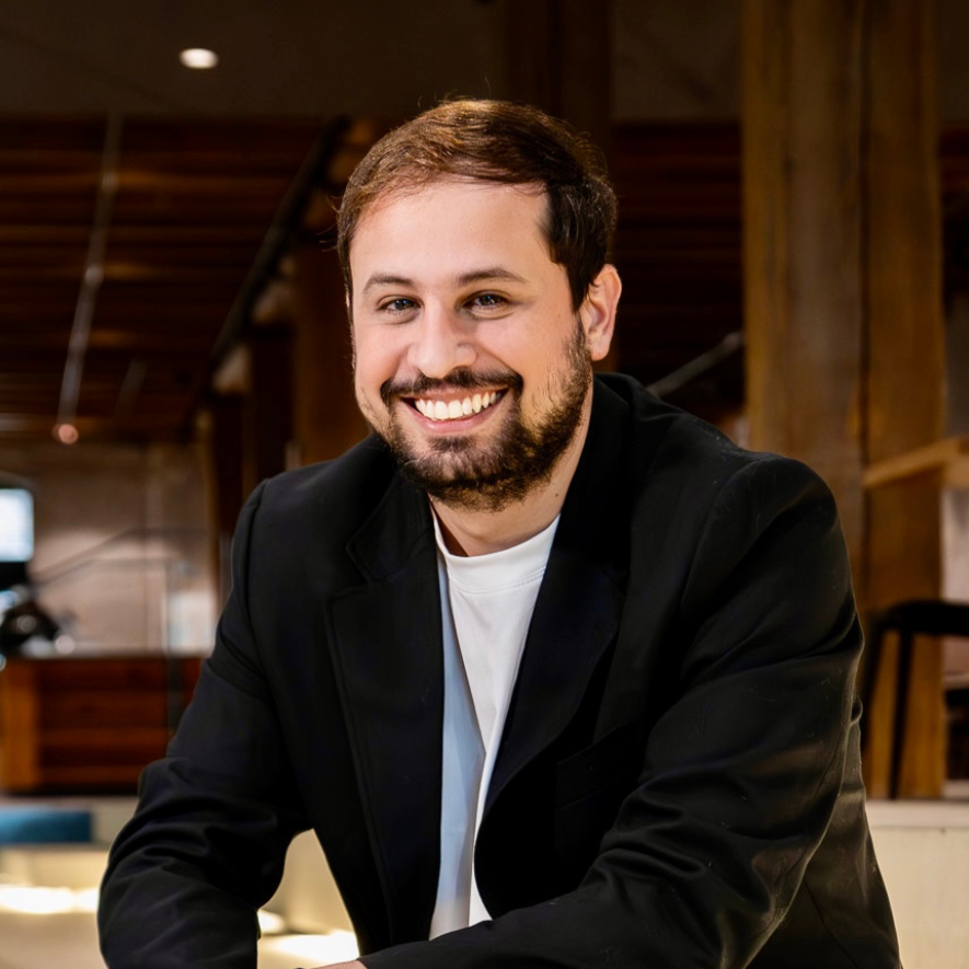 A man with a beard is wearing a black jacket and smiling for the camera.