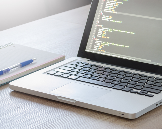 A laptop is open on a desk next to a notebook and pen